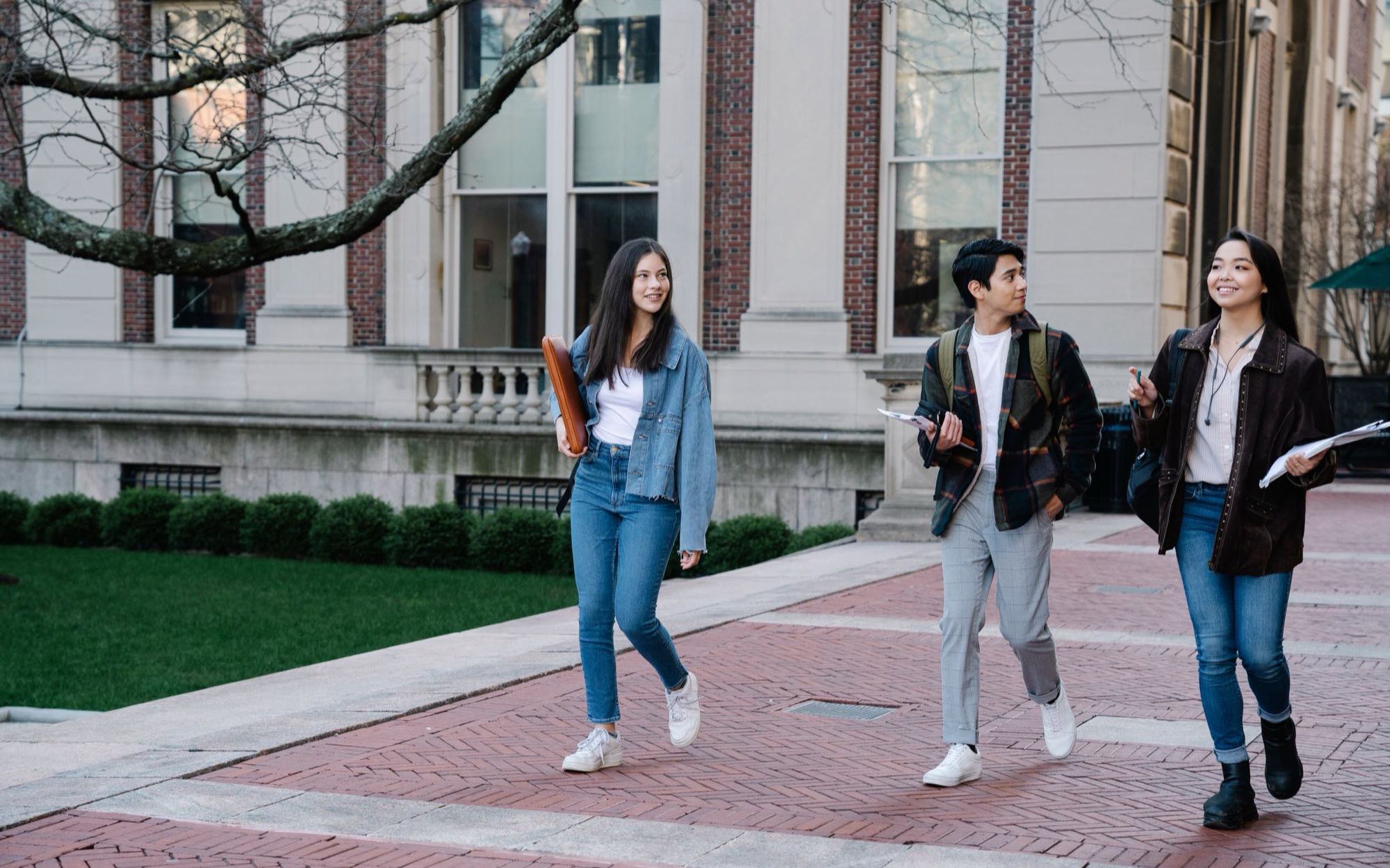 Three university students walking together across a campus courtyard between brick faculty buildings